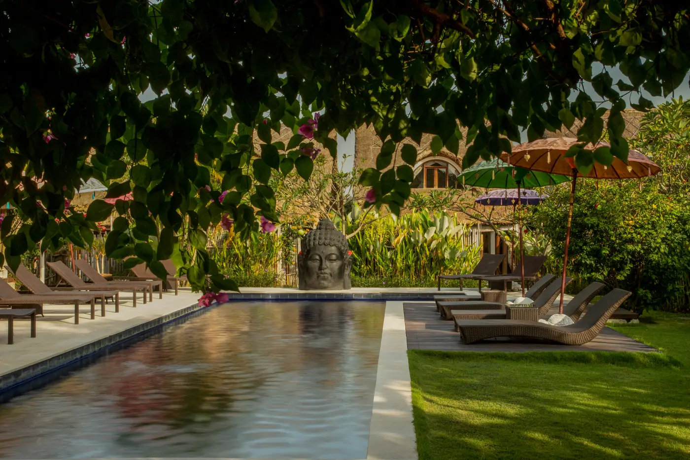 Piscine des villas United Colors of Bali à Canggu, bordée de transats et d'une tête de Bouddha