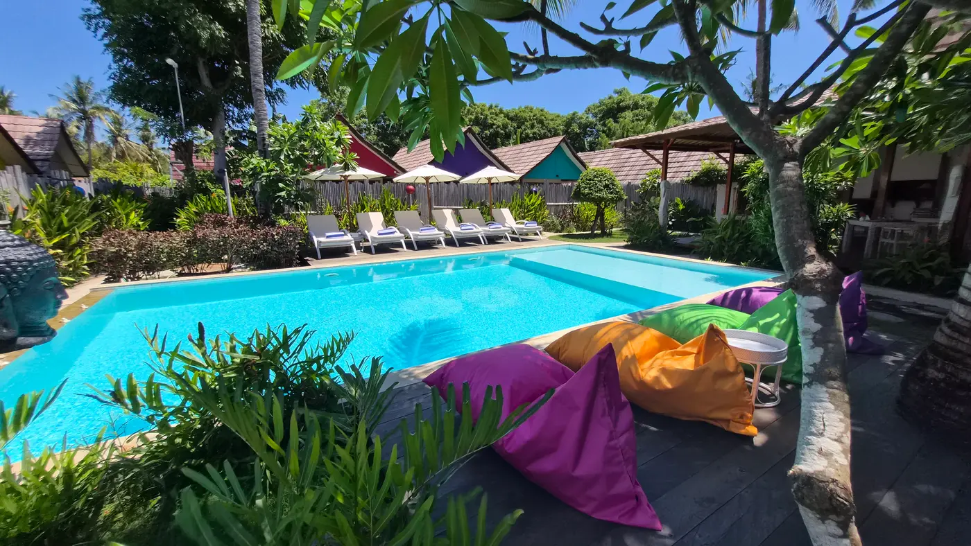 Piscine de United Colors of Gili, poufs colorés, transats et bungalows sous les frangipaniers
